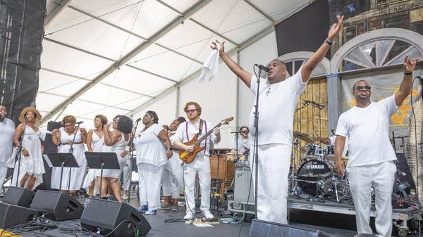 A band of people on a stage all wearing white.