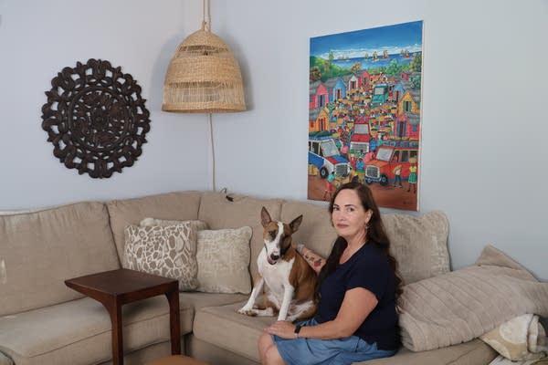 A woman poses for a photo on a tan couch next to her brown and white dog.