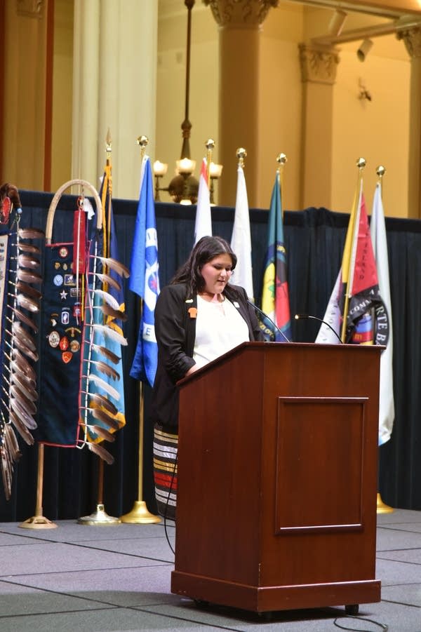 A woman speaks at a podium in front of various flags.