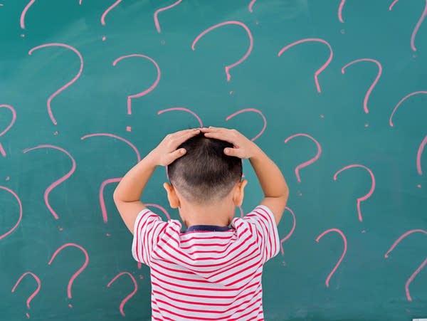 A boy in front of blackboard with question marks.