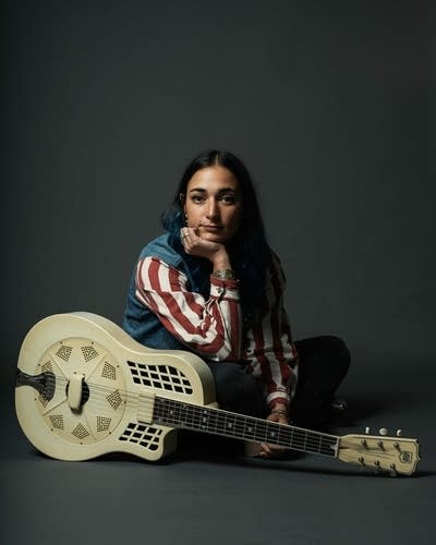 A woman poses for a studio portrait with her resonator guitar