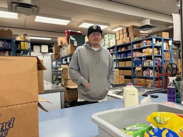 A man in a gray hoodie stands at a table inside a food shelf.