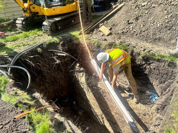 A construction worker lowers a copper line into a hole in the ground.