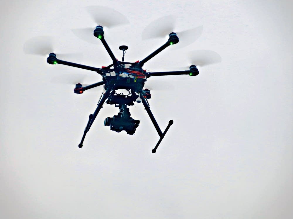 A drone rises into a gray sky.