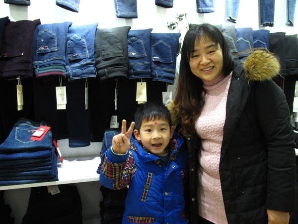Zhang Xiaoyan and her son stand in front of a wall in her clothes shop.