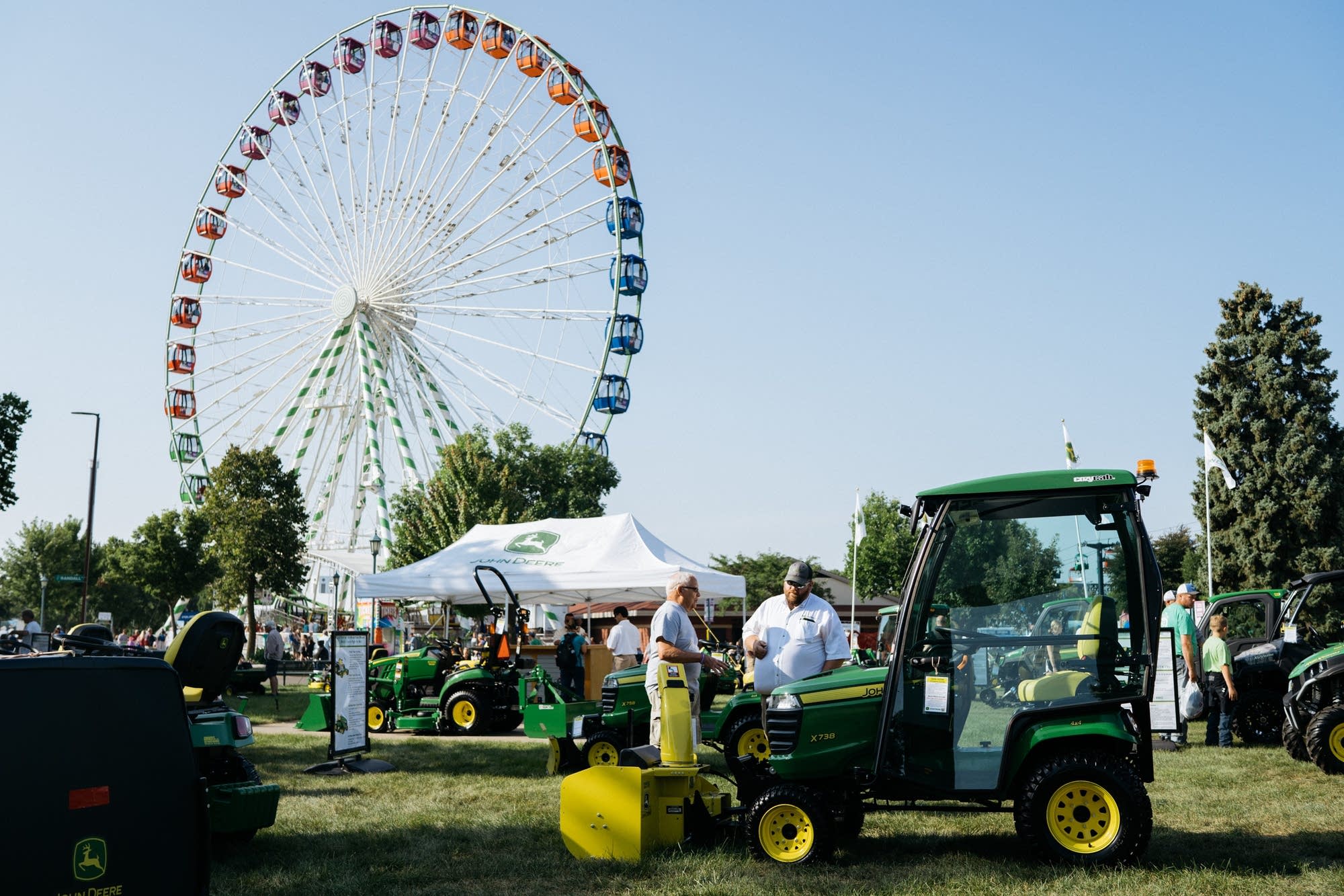 A ferris wheel turns as people check out John Deere tractors.
