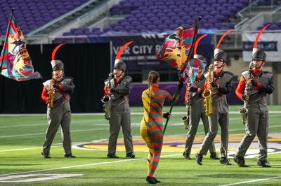 A marching band performs on the field of a football stadium.
