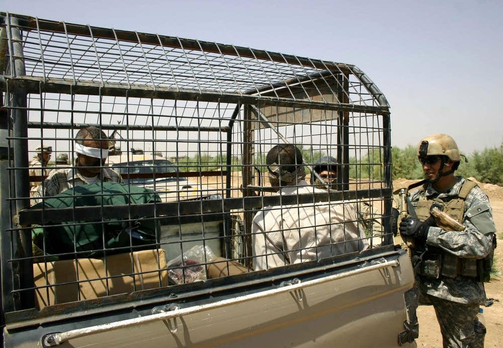 A US Marine secures two prisoners inside the back