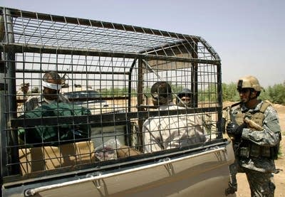 A US Marine secures two prisoners inside the back