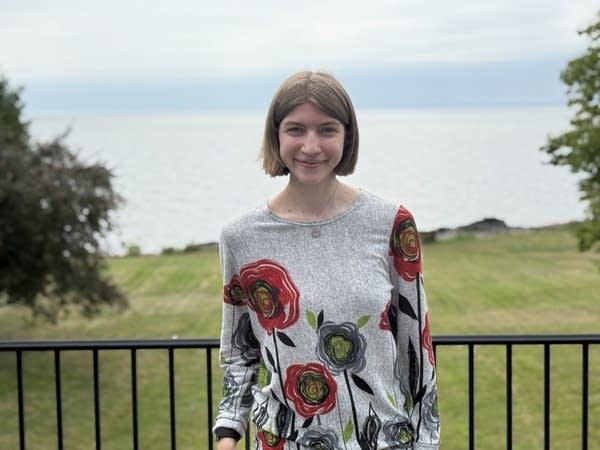 A woman in a floral shirt poses on a balcony overlooking a large yard.