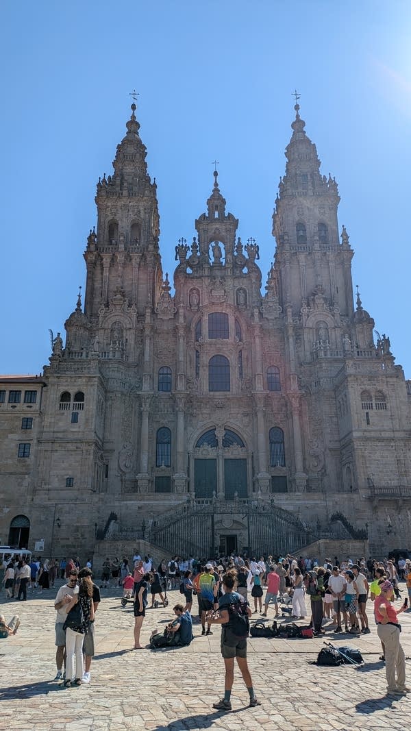 An ornate cathedral. Hikers crowd a plaza in front of the tall building.