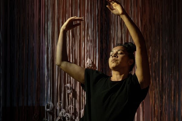 A woman in black poses with her arms in the air