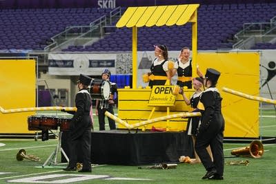 A marching band performs on the field of a football stadium.