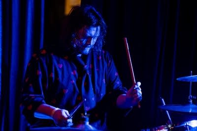 A musician plays drums onstage in a music venue