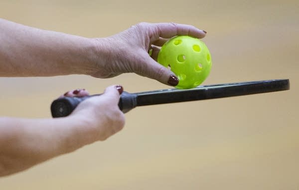 A close up of a hands holding a green ball and a paddle. 