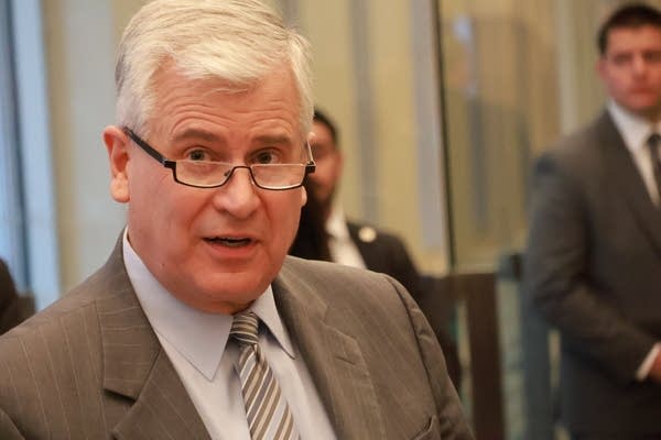 man with reading glasses and gray tie speaks in courthouse lobby
