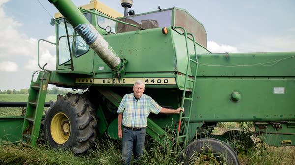 An older man stands in front of a huge green combine