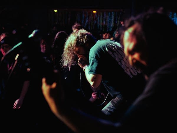 A person sings forcefully into a microphone.