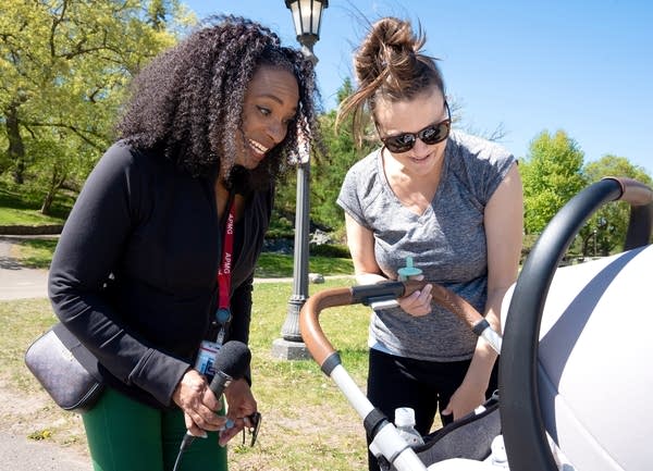 two women smile as they look into a baby carriage