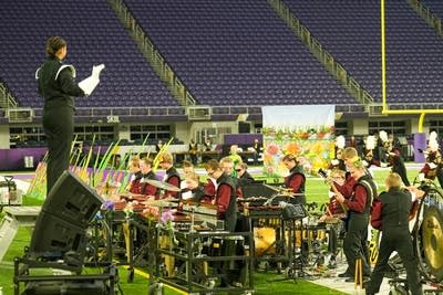 A marching band performs on the field of a football stadium.