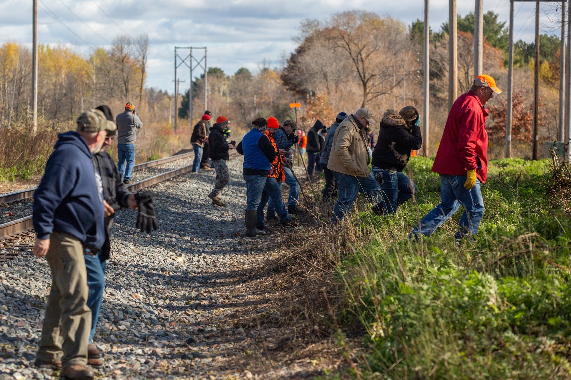Volunteers make their way in a line across train tracks.