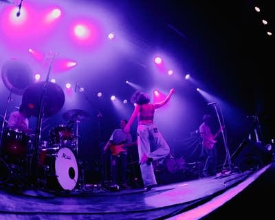 A woman dances with a band playing nearby on a lighted stage.