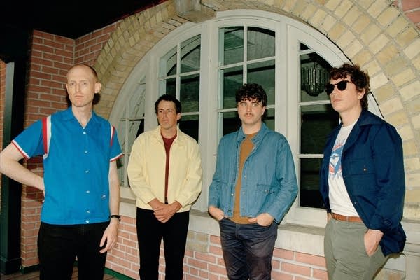 Four guys stand in front of a semicircular window in a brick building