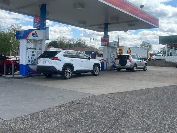 A white SUV and a silver hatchback are parked at a gas pump.