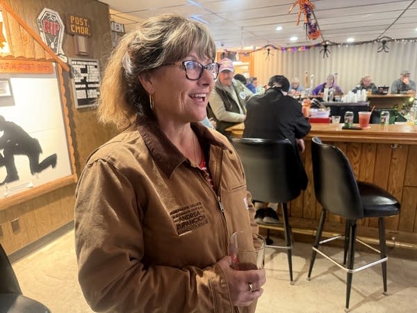 A woman holds a drink and talks to people at a local VFW bar.
