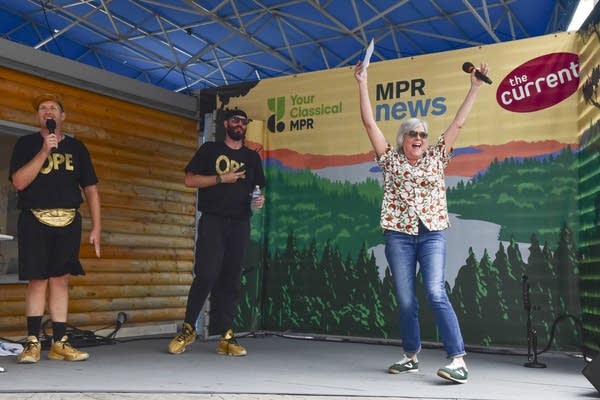 Three people with microphones onstage at a fair