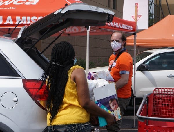 A person wearing a face mask helps load a car. 