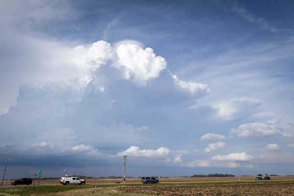 Puffy, white clouds are seen in a dark blue sky hanging over a rural road.