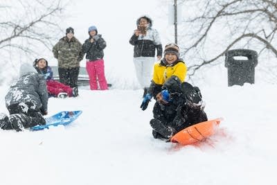 Sledders ride down a snowy hill.