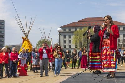 A woman in red holds a microphone and speaks