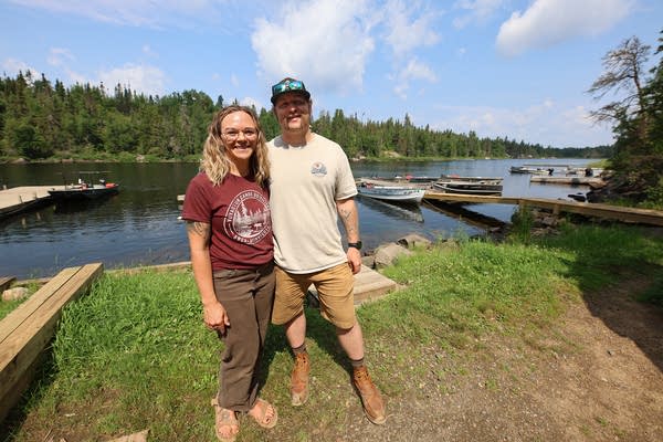 A man and woman pose for a photo in front of docks on a lake.