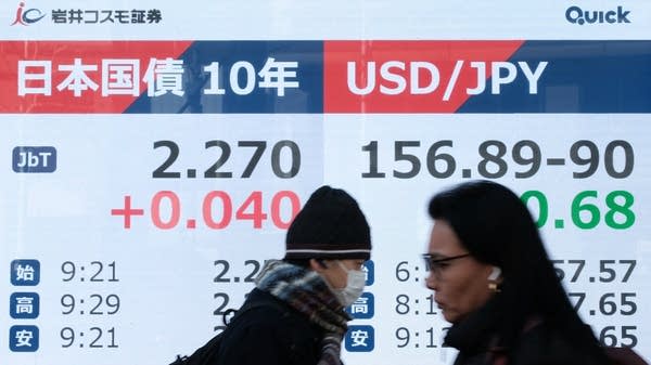 Pedestrians walk past an electronic quotation boards displaying 10-year government bond yields and other financial data points in Tokyo.