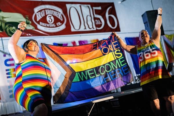 Two performers wearing rainbow outfits hold a pride flag