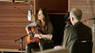 A woman sings and plays guitar in a recording studio