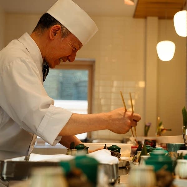 A chef holds chopsticks while preparing plates in a warmly-lit restaurant