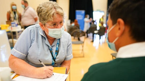 NEWCASTLE UPON TYNE, ENGLAND - SEPTEMBER 22: Felix Dima, 13, from Newcastle speaks with a nurse before he receives the Pfizer-BioNTech COVID-19 vaccine at the Excelsior Academy on September 22, 2021 in Newcastle upon Tyne, England.  The Excelsior Academy on Denton Road in Newcastle is the first school in the North East and North Cumbria to offer the Pfizer-BioNTech COVID-19 vaccination to healthy 12-15-year-olds where parents have provided consent. This week the NHS and local School Age Vaccination Services begin immunising children aged 12 to 15 on advice from the UK's four Chief Medical Officers, in a move to reduce the disruption to education caused by COVID-19. The Medicines and Healthcare products Regulatory Agency (MHRA) confirmed that the Pfizer vaccine is safe and effective for 12 to 17-year-olds. (Photo by Ian Forsyth/Getty Images)
