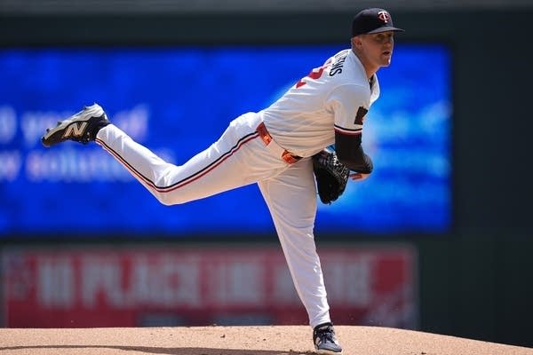 A baseball pitcher leans forward and lifts his leg after throwing the ball.