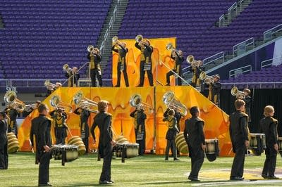 A marching band performs on the field of a football stadium.