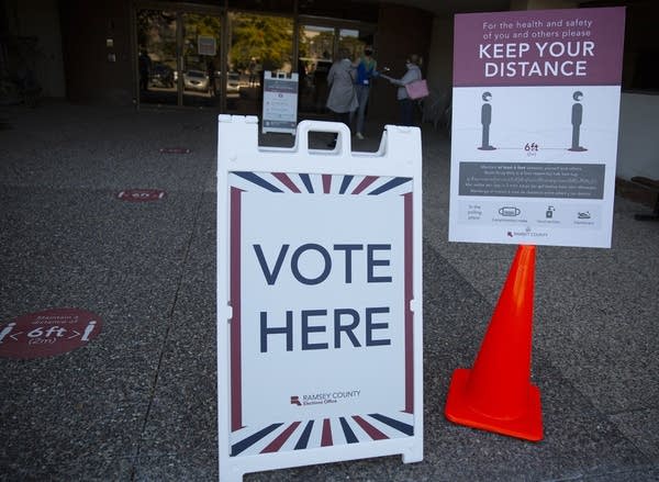 A sign that reads "vote here" and a sign that reads "keep your distance."