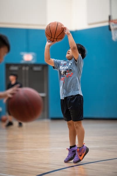 A young boy stands on his toes to shoot a basketball.