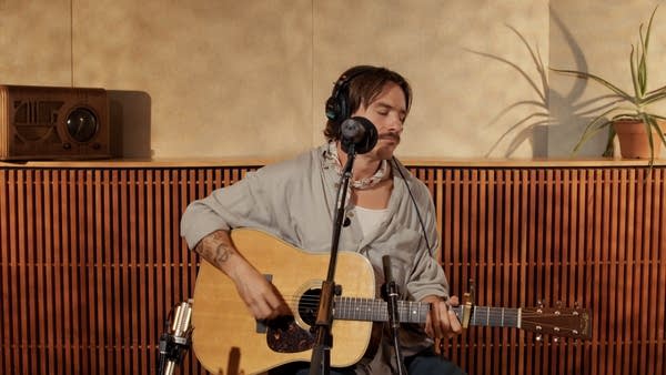 A musician sings and plays guitar in a recording studio