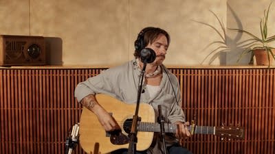 A musician sings and plays guitar in a recording studio