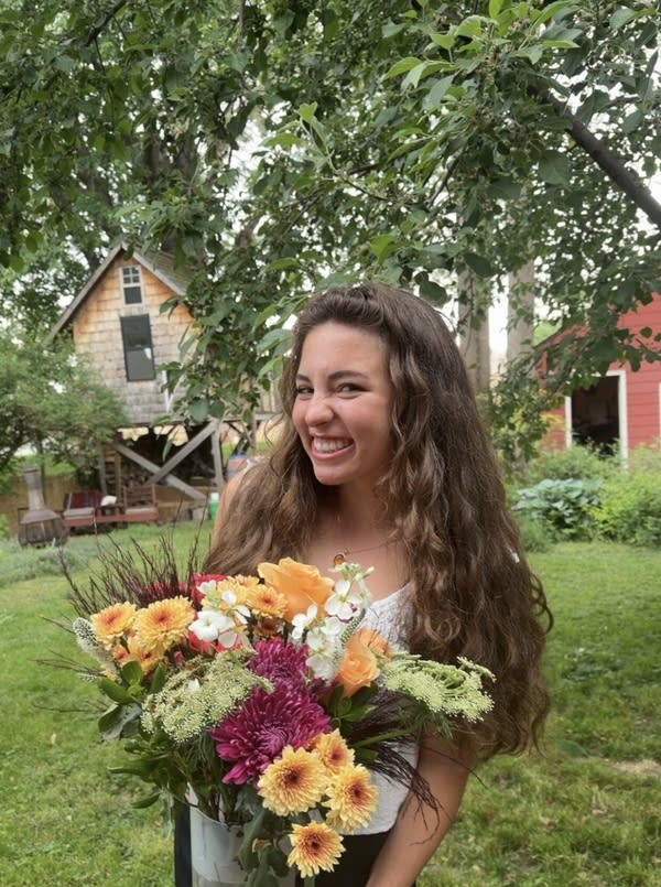 A woman smiles for a photo while holding a bouquet of flowers.
