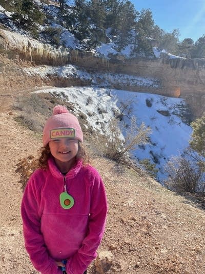 A young girl in pink smiles near a lake