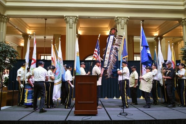 A group of people in military uniforms stand on a stage holding various flags.