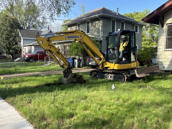 A yellow excavator digs in a house's yard.